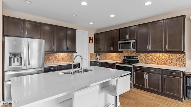 kitchen with light wood finished floors, a sink, dark brown cabinetry, appliances with stainless steel finishes, and light countertops