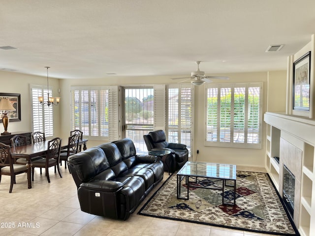 tiled living room featuring a fireplace and ceiling fan with notable chandelier