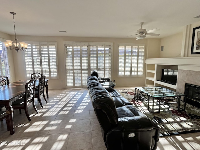 tiled living room with a tiled fireplace, ceiling fan with notable chandelier, and plenty of natural light