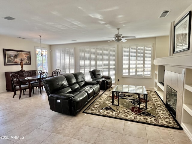 tiled living room with ceiling fan with notable chandelier and a fireplace