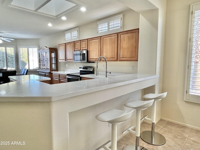 kitchen with sink, appliances with stainless steel finishes, a kitchen bar, light tile patterned flooring, and kitchen peninsula