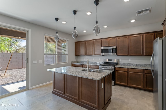 kitchen with a kitchen island with sink, sink, appliances with stainless steel finishes, decorative light fixtures, and light stone counters