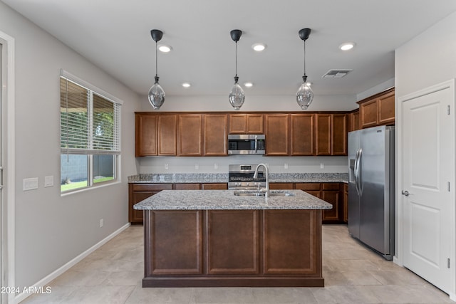 kitchen with hanging light fixtures, light stone countertops, stainless steel appliances, and a kitchen island with sink