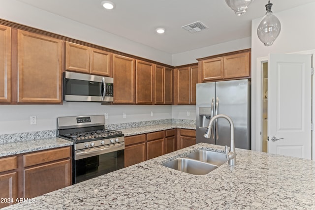 kitchen with stainless steel appliances, light stone counters, hanging light fixtures, and sink