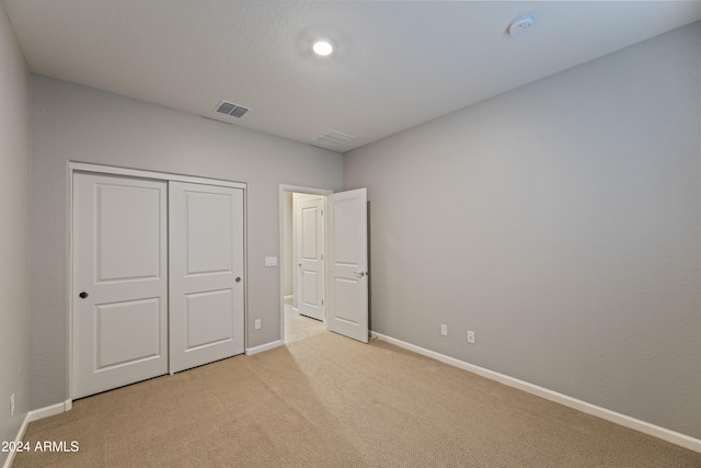 unfurnished bedroom with light colored carpet and a closet