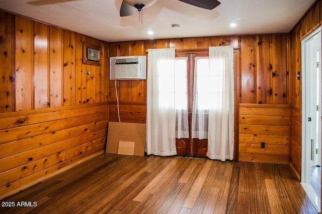 unfurnished bedroom with a wall mounted air conditioner, ceiling fan, wooden walls, and hardwood / wood-style floors