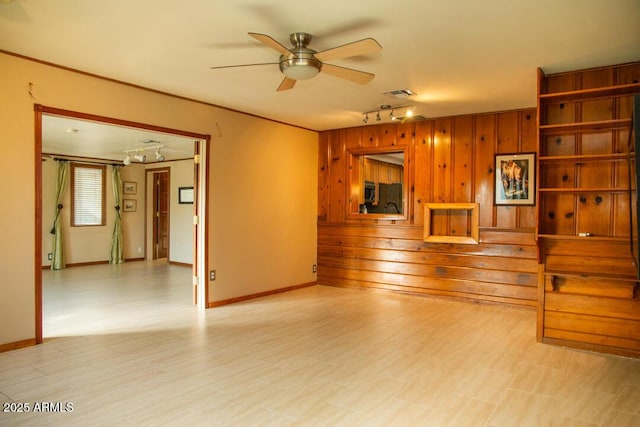 unfurnished living room featuring ceiling fan, wood walls, and track lighting