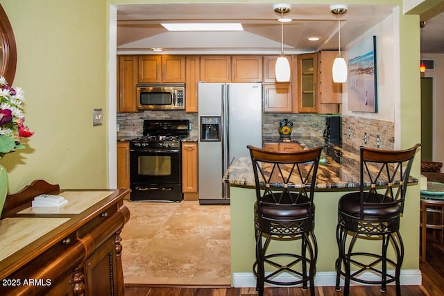 kitchen with pendant lighting, appliances with stainless steel finishes, dark stone countertops, backsplash, and a breakfast bar area