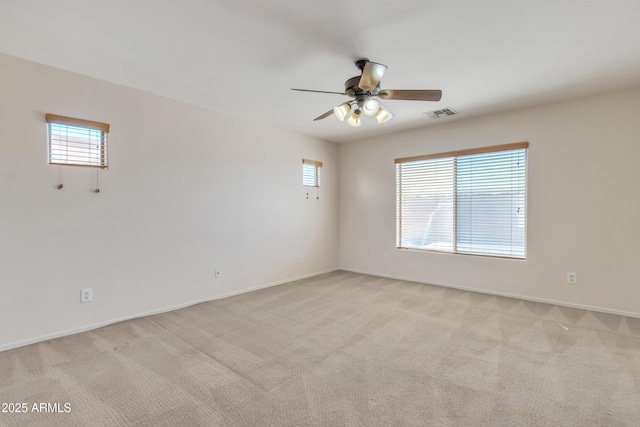 spare room featuring light colored carpet, ceiling fan, visible vents, and a wealth of natural light