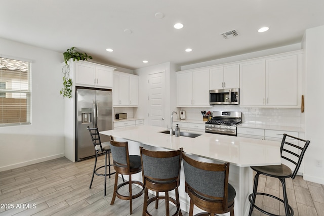kitchen featuring a sink, appliances with stainless steel finishes, decorative backsplash, white cabinets, and light wood-style floors