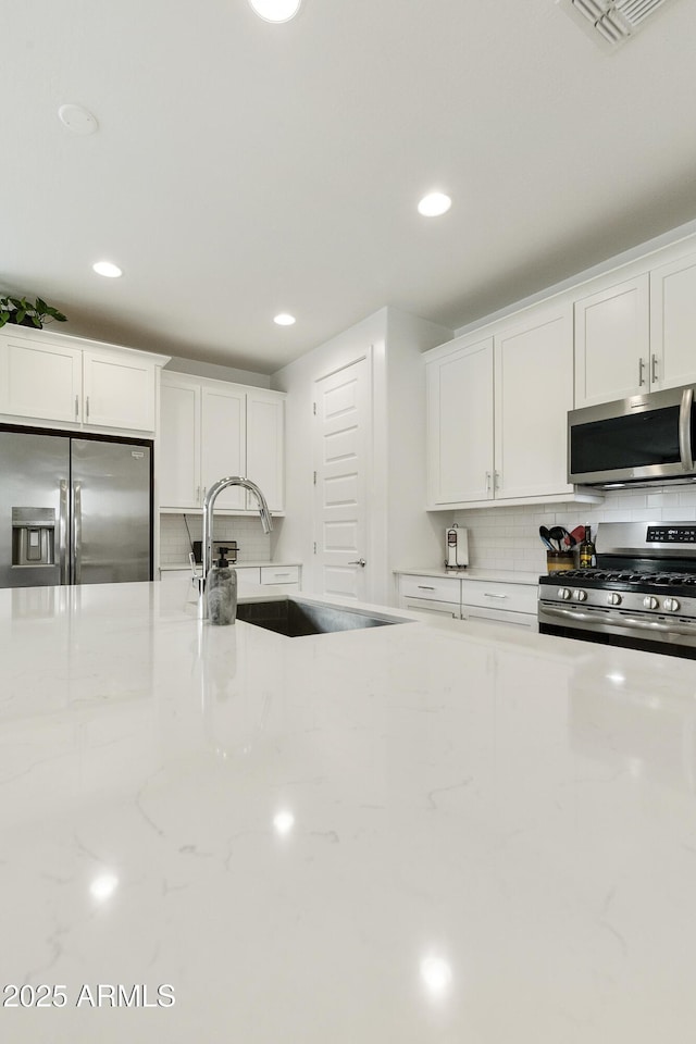 kitchen with white cabinets, appliances with stainless steel finishes, decorative backsplash, and a sink