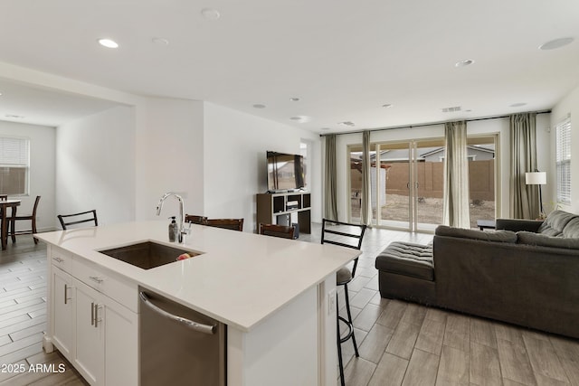 kitchen with a sink, dishwasher, a kitchen bar, open floor plan, and light countertops