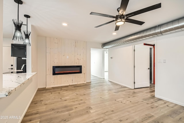 unfurnished living room with heating unit, ceiling fan, a fireplace, and light hardwood / wood-style flooring