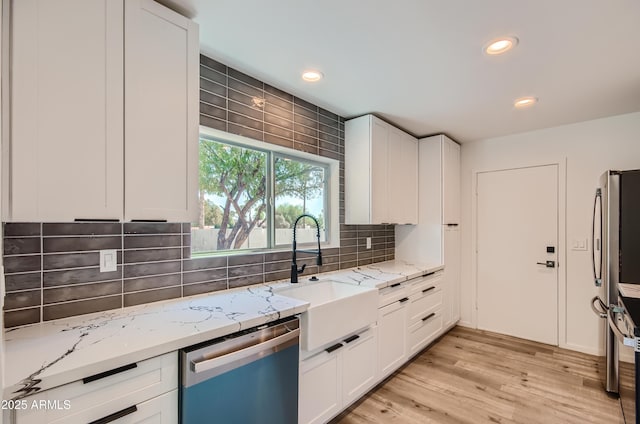 kitchen with white cabinetry, stainless steel appliances, sink, and light stone counters