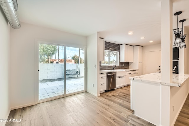 kitchen featuring white cabinets, decorative backsplash, stainless steel dishwasher, light stone counters, and light wood-type flooring