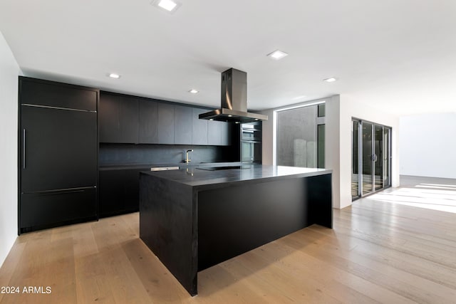 kitchen featuring island exhaust hood, black stovetop, light hardwood / wood-style floors, a center island, and backsplash