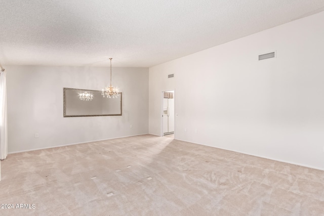 spare room featuring a notable chandelier, a textured ceiling, and light colored carpet