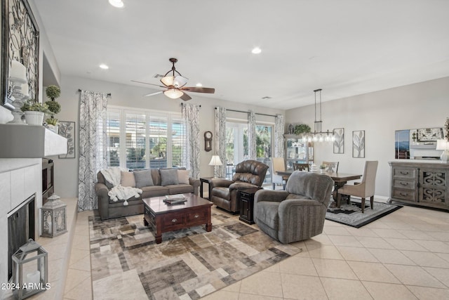 living room featuring ceiling fan with notable chandelier, a wealth of natural light, light tile patterned floors, and a fireplace