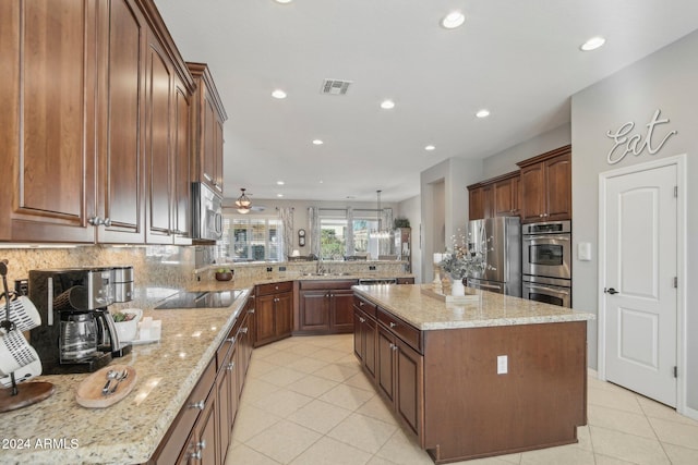 kitchen with pendant lighting, light stone countertops, a kitchen island, and appliances with stainless steel finishes