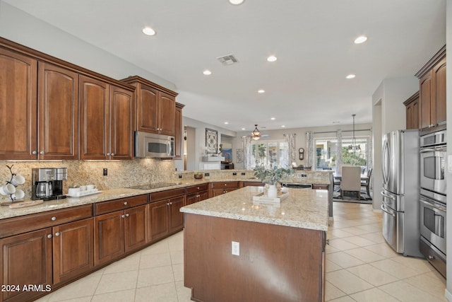 kitchen featuring appliances with stainless steel finishes, kitchen peninsula, light stone countertops, decorative light fixtures, and a center island