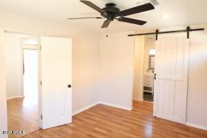 unfurnished bedroom featuring ceiling fan, light hardwood / wood-style floors, a barn door, and ensuite bath