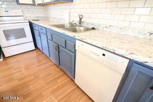 kitchen with light hardwood / wood-style floors, decorative backsplash, blue cabinetry, white appliances, and sink