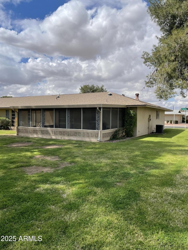 back of property with cooling unit, a yard, roof with shingles, and a sunroom