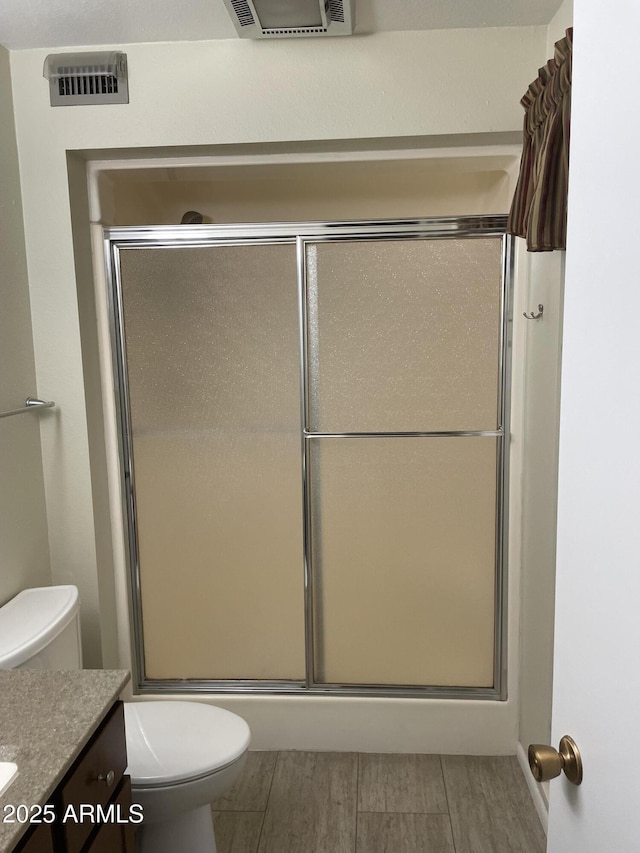 bathroom featuring vanity, toilet, visible vents, and a shower with shower door