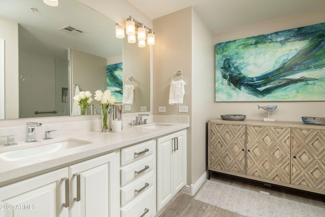 full bathroom with double vanity, wood finished floors, visible vents, and a sink