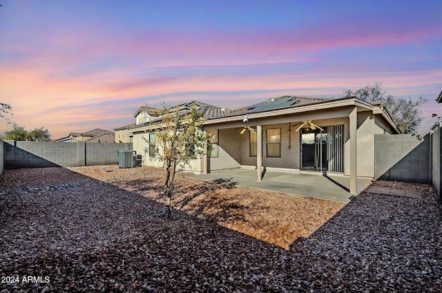 back house at dusk with a patio area, ceiling fan, cooling unit, and solar panels