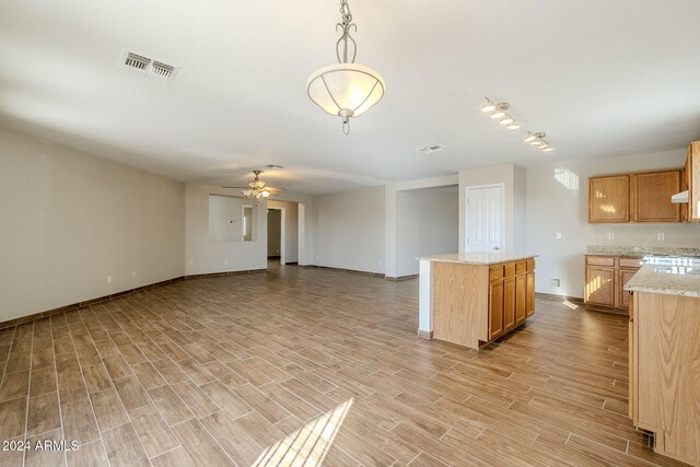 kitchen with light wood-type flooring, light stone counters, ceiling fan, decorative light fixtures, and a center island