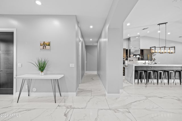 hallway with vaulted ceiling, an inviting chandelier, and sink