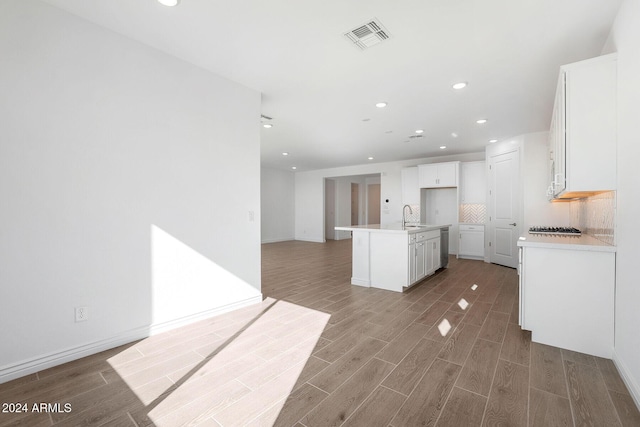 kitchen featuring sink, tasteful backsplash, hardwood / wood-style floors, an island with sink, and white cabinets