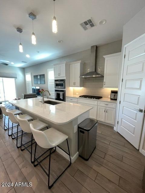 kitchen with decorative light fixtures, sink, wall chimney range hood, and white cabinets