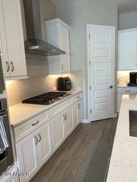 kitchen featuring appliances with stainless steel finishes, dark hardwood / wood-style floors, light stone countertops, wall chimney exhaust hood, and white cabinets