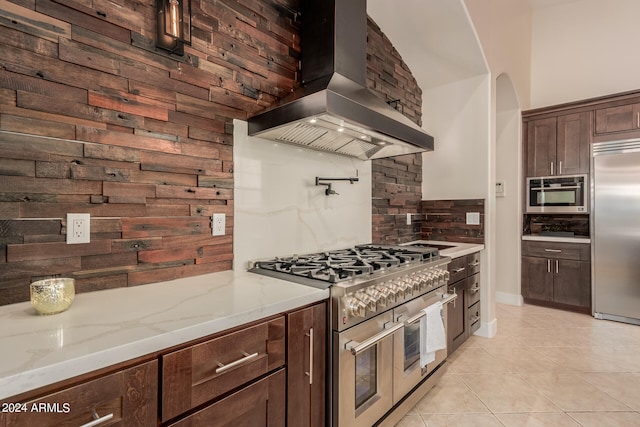 kitchen with decorative backsplash, wall chimney exhaust hood, light stone countertops, premium appliances, and light tile patterned floors