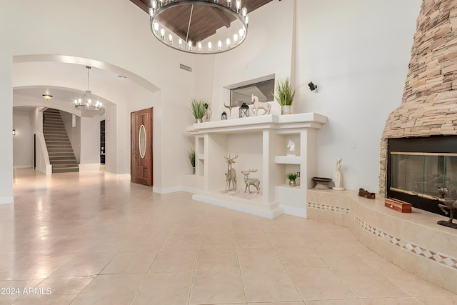 unfurnished living room featuring light tile patterned floors, a stone fireplace, a chandelier, and a high ceiling