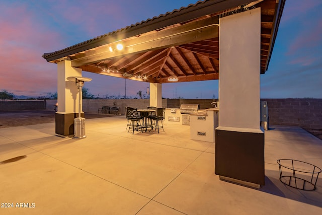 patio terrace at dusk with an outdoor kitchen, a gazebo, and a grill