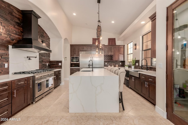 kitchen featuring lofted ceiling, high end appliances, tasteful backsplash, a kitchen island with sink, and wall chimney exhaust hood