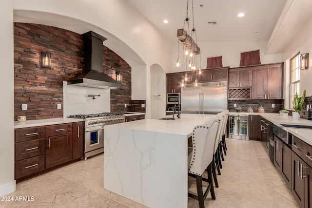 kitchen featuring backsplash, premium appliances, a kitchen island with sink, sink, and wall chimney range hood