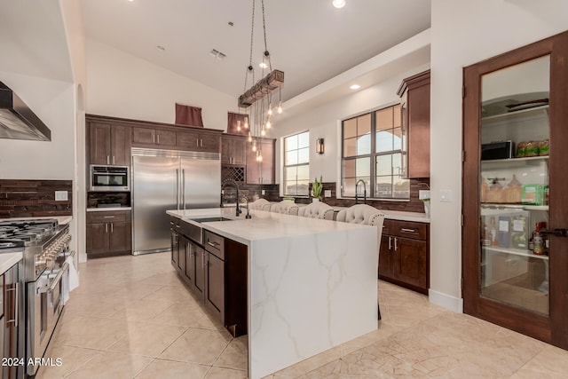 kitchen with a kitchen island with sink, decorative backsplash, decorative light fixtures, and high quality appliances