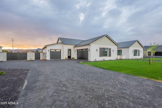 modern farmhouse style home featuring a gate, decorative driveway, fence, an attached garage, and a front yard