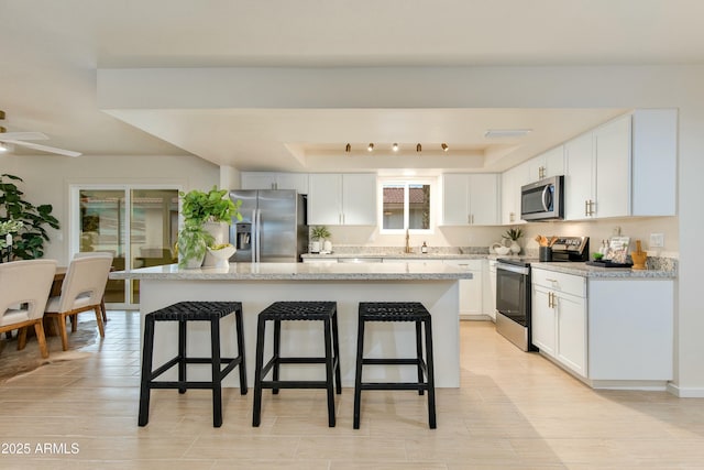 kitchen featuring a kitchen island, a breakfast bar, appliances with stainless steel finishes, white cabinets, and a raised ceiling