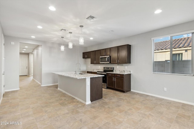 kitchen featuring hanging light fixtures, appliances with stainless steel finishes, a kitchen island with sink, dark brown cabinetry, and sink