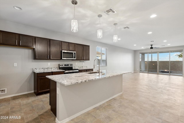 kitchen with a center island with sink, light stone counters, appliances with stainless steel finishes, pendant lighting, and sink