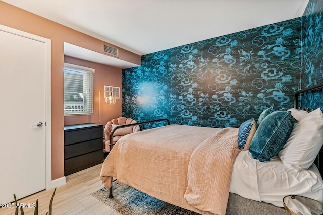 bedroom with wallpapered walls, baseboards, visible vents, and wood finished floors