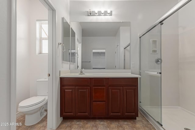 bathroom featuring a shower with door, vanity, and toilet