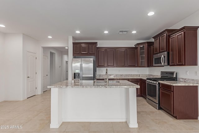 kitchen featuring sink, dark brown cabinets, stainless steel appliances, light stone counters, and an island with sink