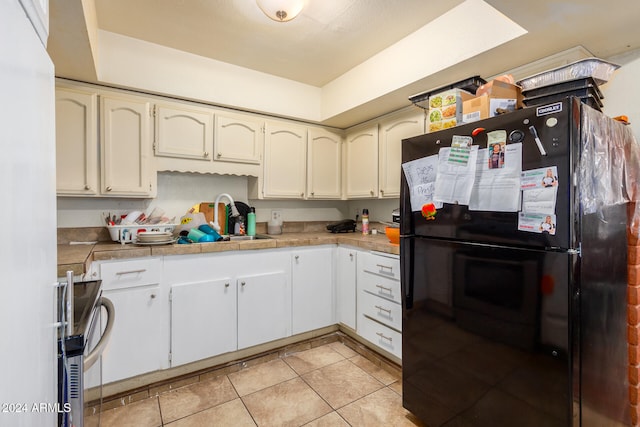 kitchen featuring light tile patterned flooring, sink, white cabinets, black refrigerator, and electric stove