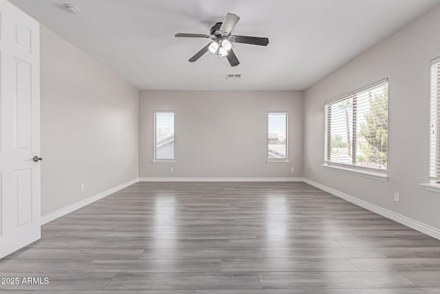 empty room with baseboards, ceiling fan, visible vents, and wood finished floors